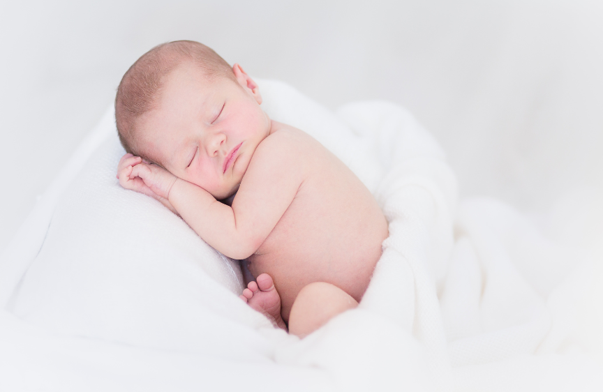 Naissance Un bébé endormi dans des draps blancs.